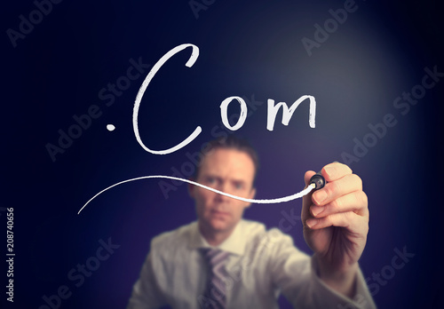 A businessman writing a Dot Com concept with a white pen on a clear screen.