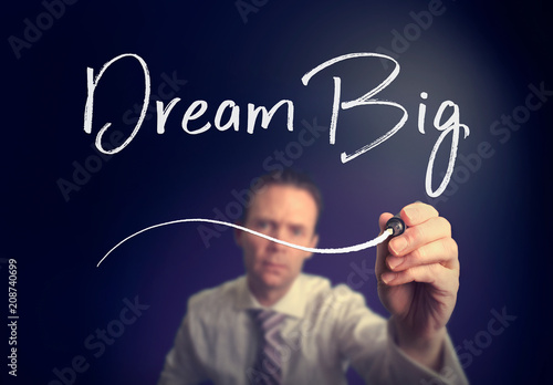 A businessman writing a Dream Big concept with a white pen on a clear screen.