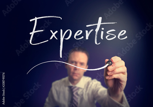 A businessman writing a Expertise concept with a white pen on a clear screen.