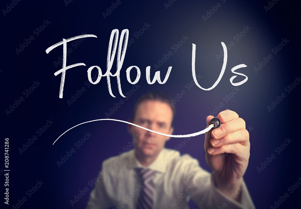 A businessman writing a Follow Us concept with a white pen on a clear screen. A businessman writing a Follow Us concept with a white pen on a clear screen.
