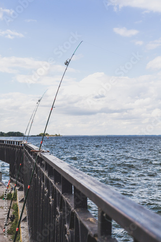 Several fishing rods leaning on fence on pier