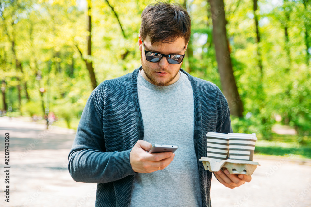 man holding coffee and phone. walking by city park. drink to go man holding coffee and phone. walking by city park. drink to go