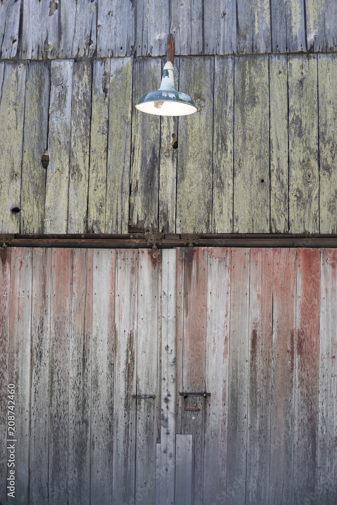 Detail of the side of a weathered barn with an old green light fixture.