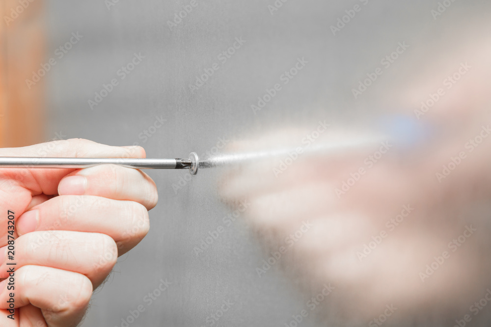 Man's hand using screwdriver at stainless surface. Employee montaging steel coating to wall or door, or other surfaces. Commercial building company concept. Man's hand using screwdriver at stainless surface. Employee montaging steel coating to wall or door, or other surfaces. Commercial building company concept.