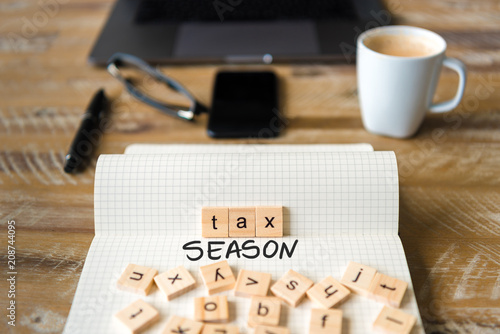 Closeup on notebook over vintage desk background, front focus on wooden blocks with letters making Tax Season text