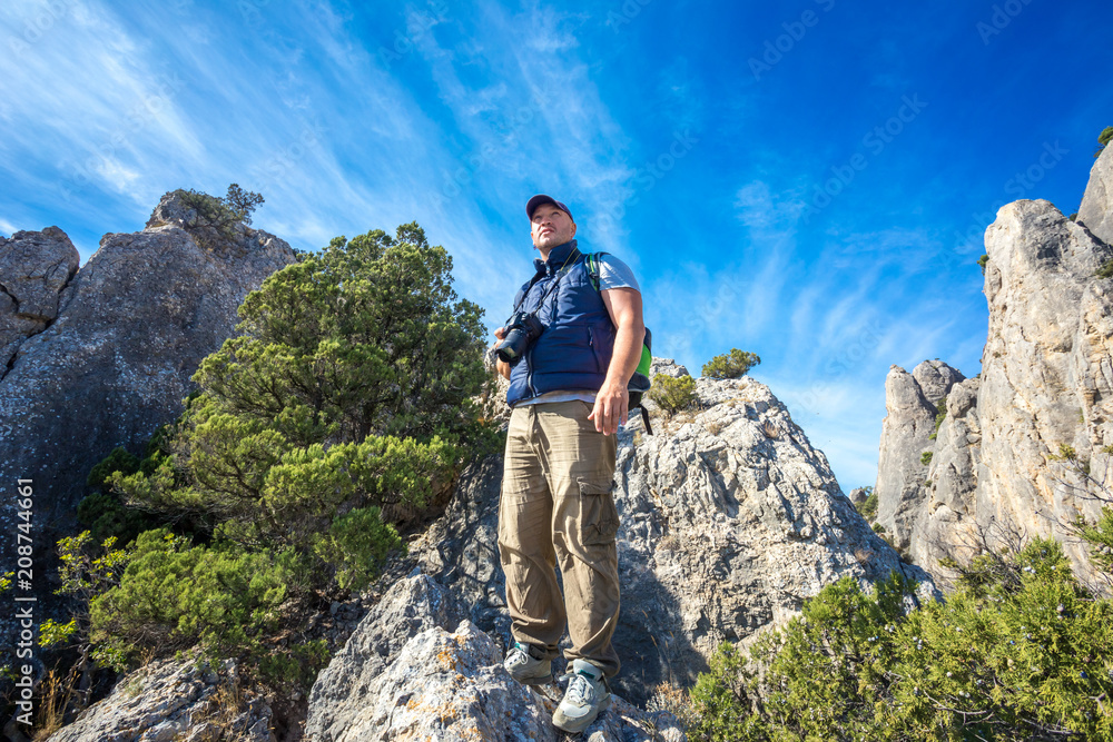 tourist looking around with camera in hand, standing on the rock, blue sky and clouds, travel concept
