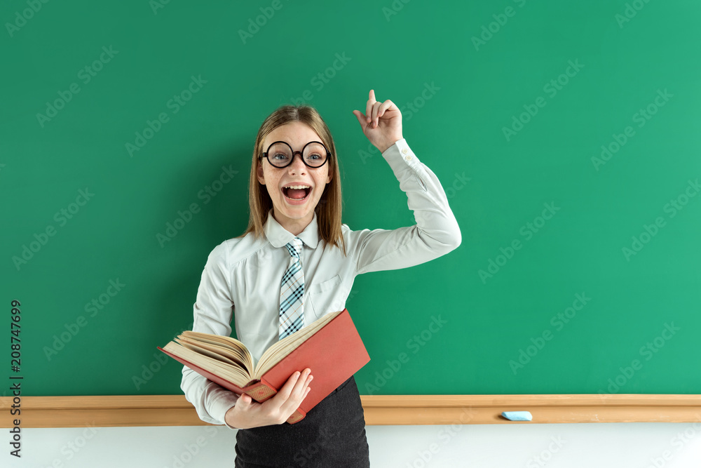 Young schoolgirl having good idea, pointing finger up and looking at camera. Refresh one's memory. Education concept Young schoolgirl having good idea, pointing finger up and looking at camera. Refresh one's memory. Education concept