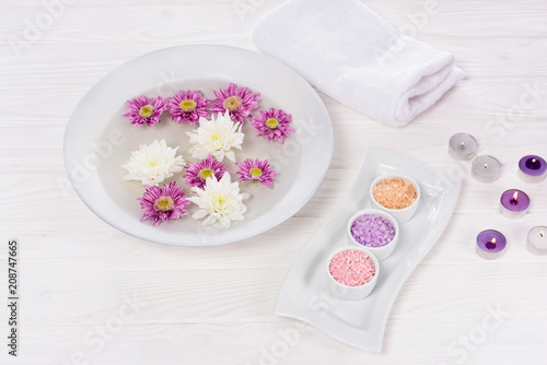 closeup view of bath for nails with flowers at table with towel, colorful sea salt and aroma candles for manicure and pedicure in beauty salon