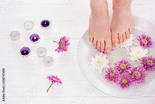 cropped shot of barefoot woman receiving bath for nails flowers near aroma candles in beauty salon