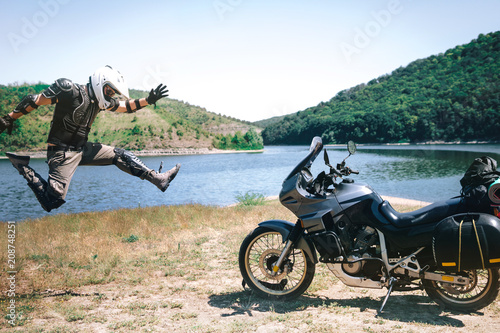 Fototapeta Naklejka Na Ścianę i Meble -  motorcycle driver rock and roll jump, adventure concept, on the dirt beach of the mountain river, enduro, off road, beautiful view, travel equipment, bags and tent, dual sport, space for text