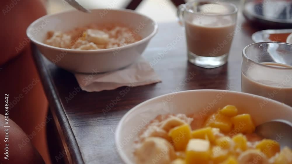 The girl behind the porridge of oatmeal porridge and mango is sitting with the phone in her hands, she is leafing through something. HD, 1920x1080, slow motion The girl behind the porridge of oatmeal porridge and mango is sitting with the phone in her hands, she is leafing through something. HD, 1920x1080, slow motion
