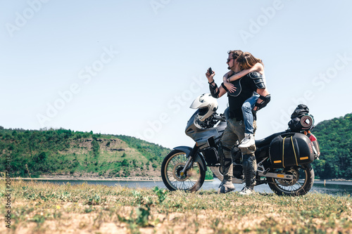 Young romantic couple having fun by the river a off road tourist motorcycle. Love, freedom, togetherness concept. Happy guy and girl travel on a motorbike, enduro touring