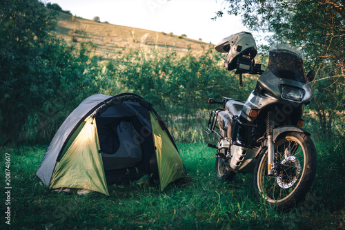 Tent and motorcycle traveler on the evening forest, sunset, enduro travel concept