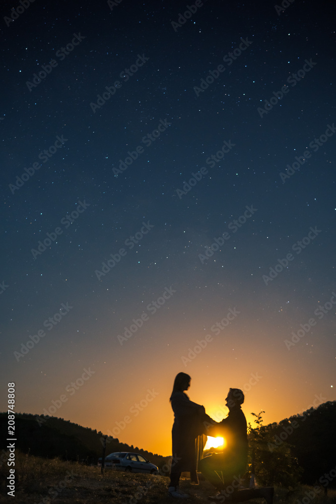 Silhouette of young couple under stars. The concept on the theme of love. romantic evening together, sunset, vertical photo, makes an offer to marry