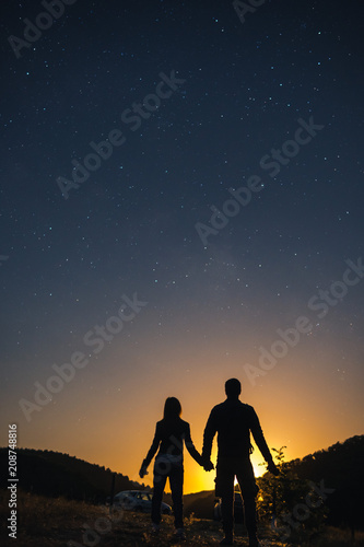 Silhouette of young couple holding hands under stars. The concept on the theme of love. romantic evening together, sunset, vertical photo