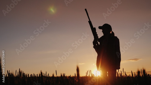 Silhouette of a woman with a gun in her hands. Hunter in the field at sunset