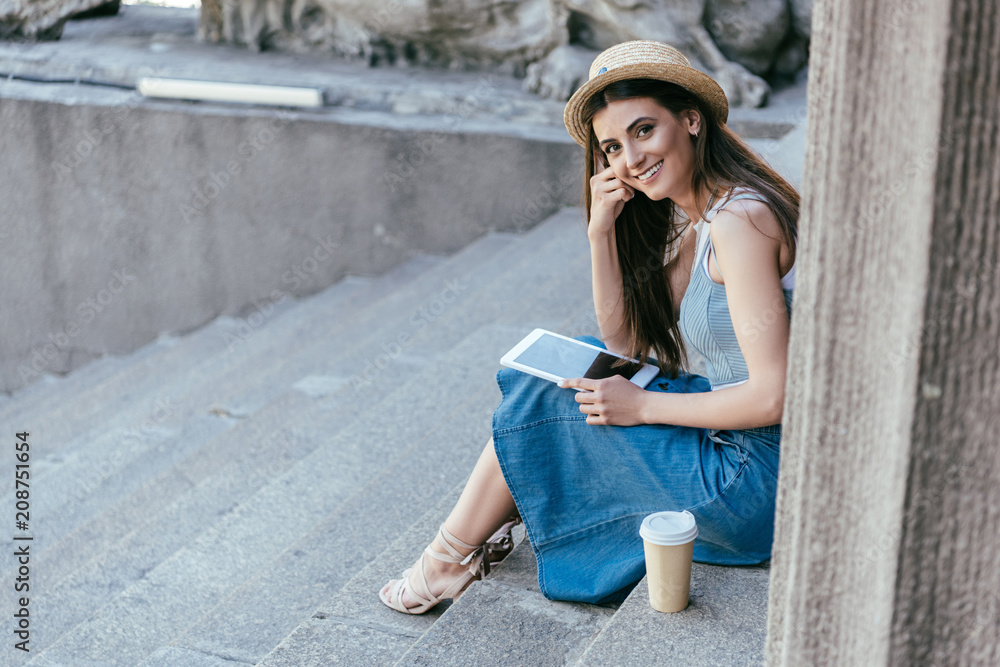 happy young woman holding digital tablet and smiling at camera while sitting on stairs happy young woman holding digital tablet and smiling at camera while sitting on stairs
