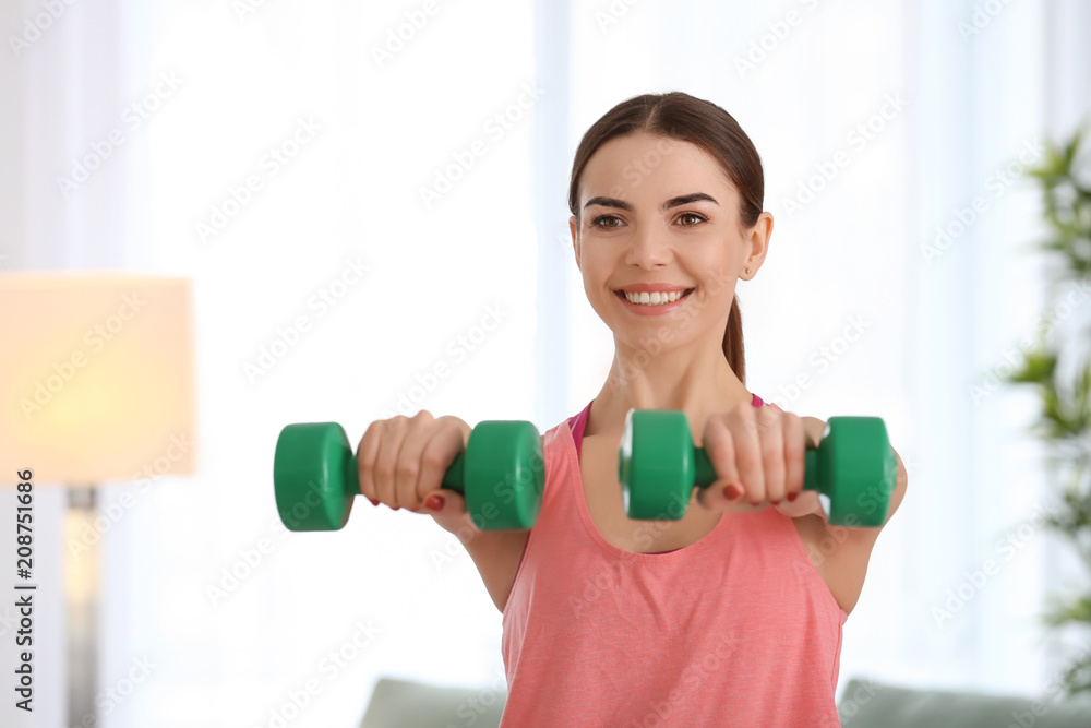 Beautiful young woman training with dumbbells at home in morning Beautiful young woman training with dumbbells at home in morning