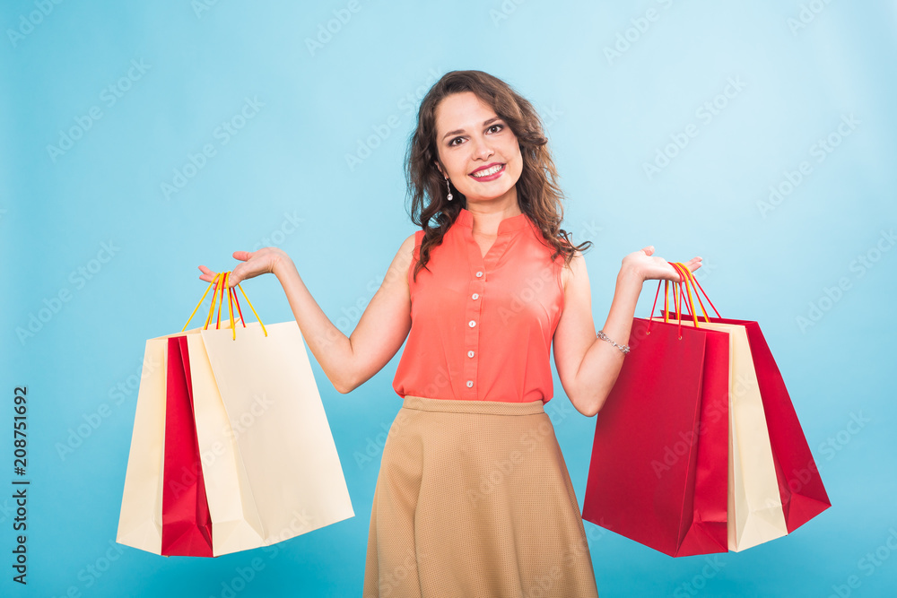 beautiful young woman with colored shopping bags over blue background
