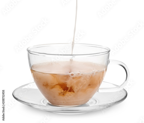 Pouring milk into glass cup with aromatic tea on white background