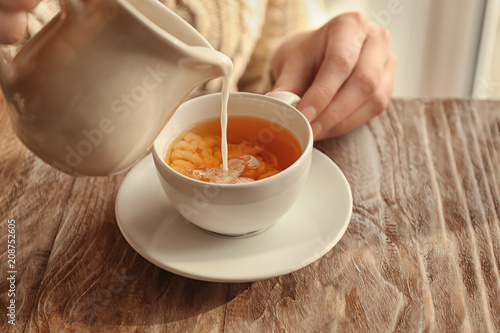 Obraz na płótnie Woman pouring milk into cup with aromatic tea on table