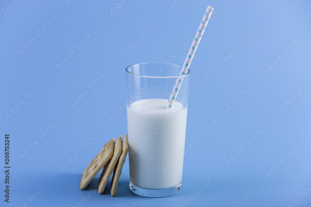 Glass of fresh cow milk with a straw and cookies on a blue background. Concept of healthy dairy products with calcium Glass of fresh cow milk with a straw and cookies on a blue background. Concept of healthy dairy products with calcium