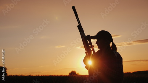 Beautiful silhouette of a woman with a rifle in the rays of the setting sun. Sports shooting and hunting concept