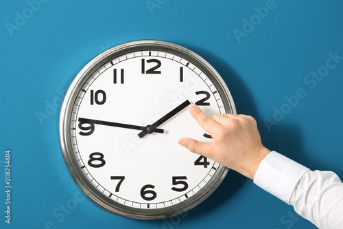 Man pointing on clock against color background. Time management concept