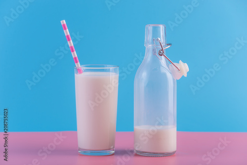 Bottle of fresh milk and a glass with a straw on a pastel background. Colorful minimalism. Healthy dairy products