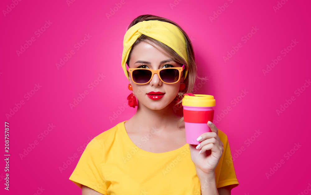 Girl in sunglasses and yellow t-shirt holding a red cup of coffee on pink background Girl in sunglasses and yellow t-shirt holding a red cup of coffee on pink background