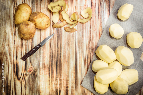 Raw peeled sliced potato, pile of potatoes and knife on rustic wooden table.