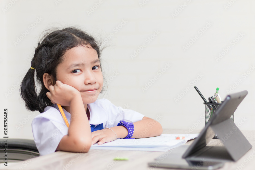 Asian little girl in student uniform doing homework and using tablet on wooden table select focus shallow depth of field Asian little girl in student uniform doing homework and using tablet on wooden table select focus shallow depth of field