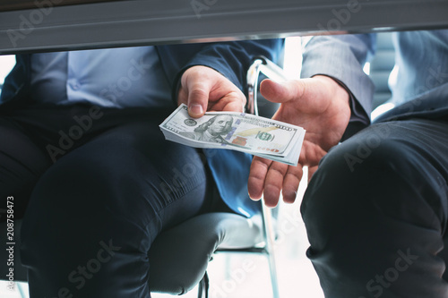 Deal. Influential rich businessman sitting next to another businessman and giving him a bribe under the table photo