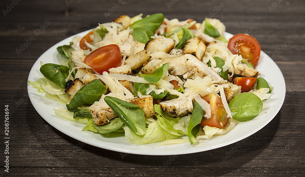 Healthy green organic Caesar salad with cheese, chicken, cherry tomatoes and croutons on a wooden table. Healthy green organic Caesar salad with cheese, chicken, cherry tomatoes and croutons on a wooden table.