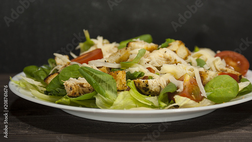 Healthy green organic Caesar salad with cheese, chicken, cherry tomatoes and croutons on a wooden table.
