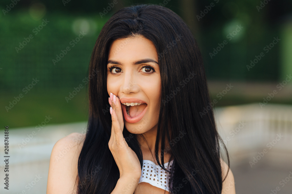 Obraz premium Happy brunette attractive female with dark hair, wonders latest news, gossips with best friend during outdoor stoll in park, has pleasant appearance, delighted expression. People and emotions