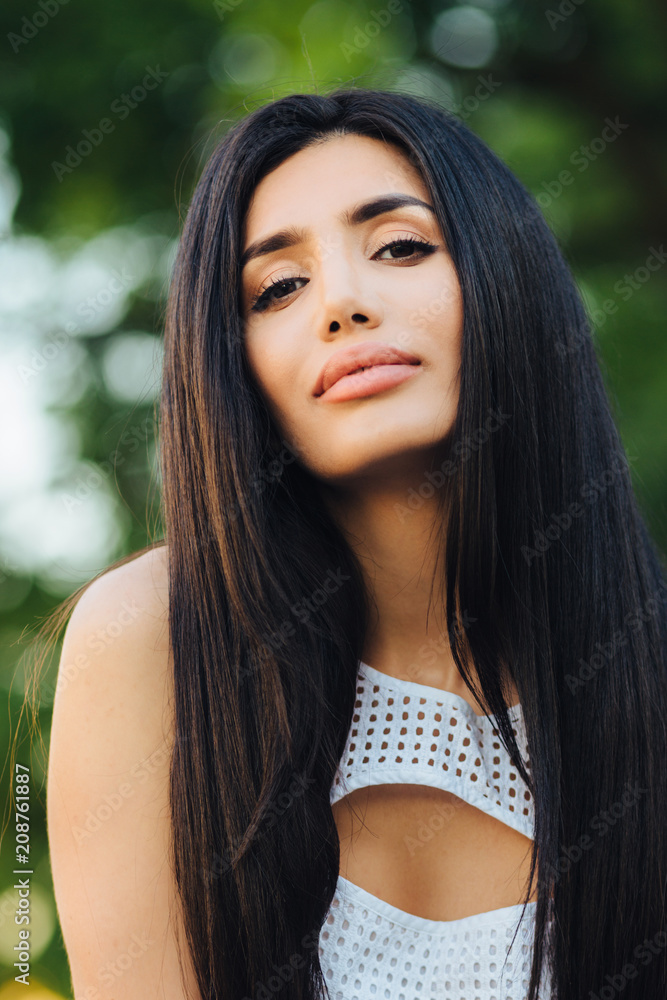 Vertical portrait of beautiful brunette woman has dark eyes, full lips and healthy skin, dressed in white dress, poses against green nature background, has pleasant specific appearance, nice make up Vertical portrait of beautiful brunette woman has dark eyes, full lips and healthy skin, dressed in white dress, poses against green nature background, has pleasant specific appearance, nice make up