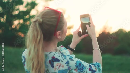 girl is photographing the sunset on the phone back view slow-mo