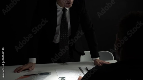 Upset interrogator talking with criminal man in dark interrogation room