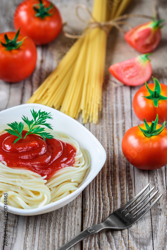 Spaghetti pasta with tomato sauce in plate and tomatoes on wooden table.