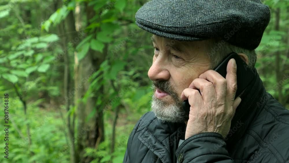 Elderly Bearded Man Talking On The Smartphone Sitting On The Bench In The Forest In Sunny Day Elderly Bearded Man Talking On The Smartphone Sitting On The Bench In The Forest In Sunny Day