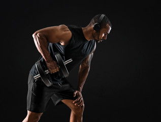 Strong handsome sport man making weightlifting and listening music on isolated black background