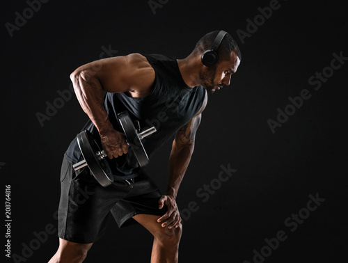 Strong handsome sport man making weightlifting and listening music on isolated black background