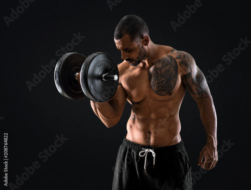 Strong handsome sport man making weightlifting and exercising the biceps on isolated black background © luismolinero