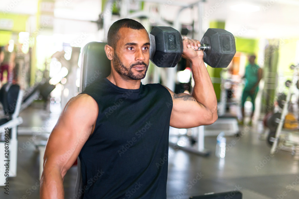 Strong handsome sport man doing shoulder exercise in the gym Strong handsome sport man doing shoulder exercise in the gym