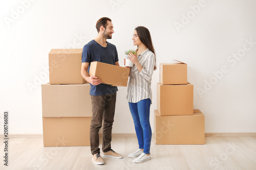 Young couple with boxes and houseplant indoors. Moving into new house © Pixel-Shot