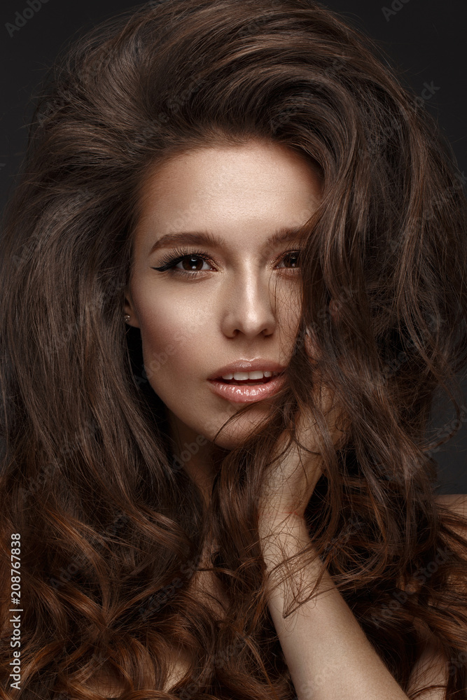 Beautiful brunette model with volume curls, classic makeup and sexy lips. The beauty of the face. Portrait shot in the studio.