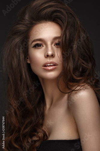 Beautiful brunette model with volume curls, classic makeup and sexy lips. The beauty of the face. Portrait shot in the studio.