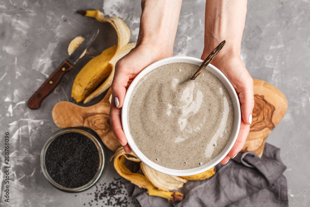 Vegan banana and black sesame milk smoothie bowl in hands for healthy breakfast. Healthy vegan food concept.