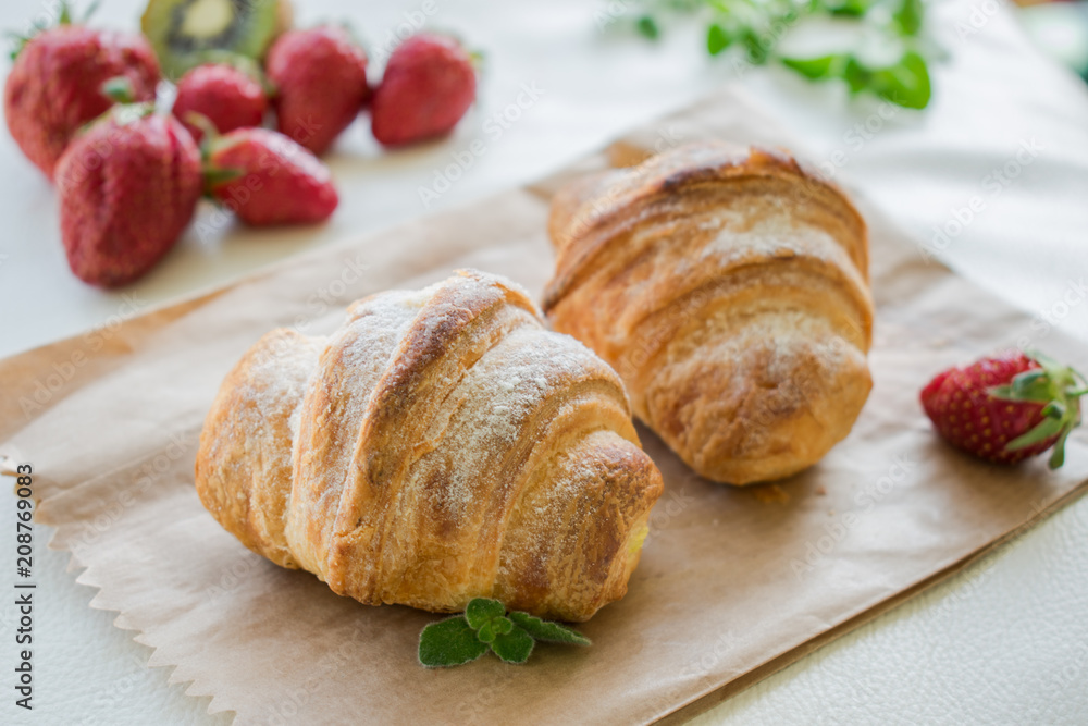 Two fresh croissants on kraft paper with strawberries in the sunlight